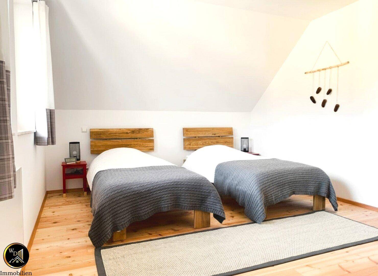 Helles Schlafzimmer im Dachgeschoss mit zwei Einzelbetten und Holzboden.
