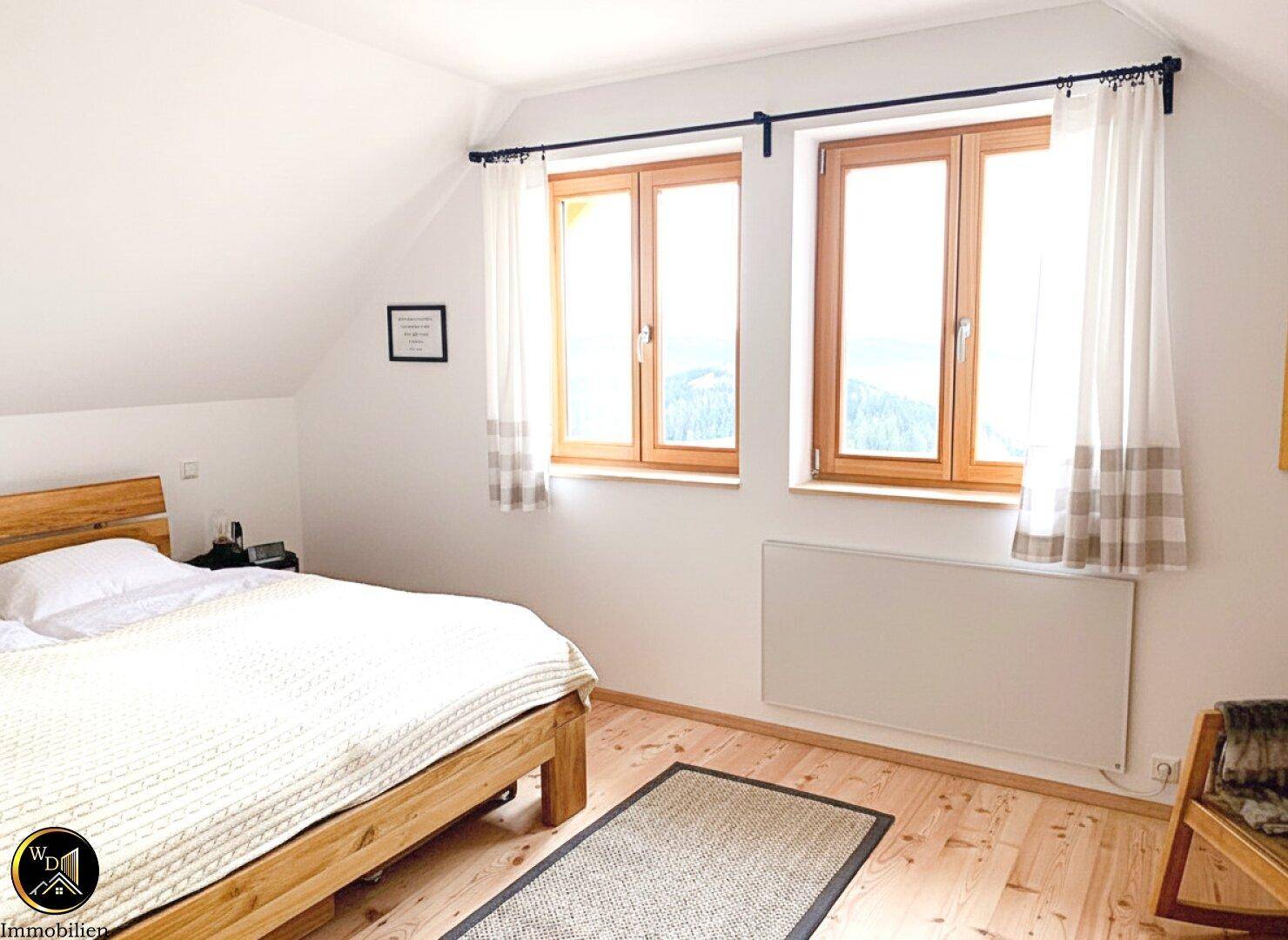 Gemütliches Schlafzimmer mit Doppelbett, Holzboden und Bergblick aus dem Fenster.