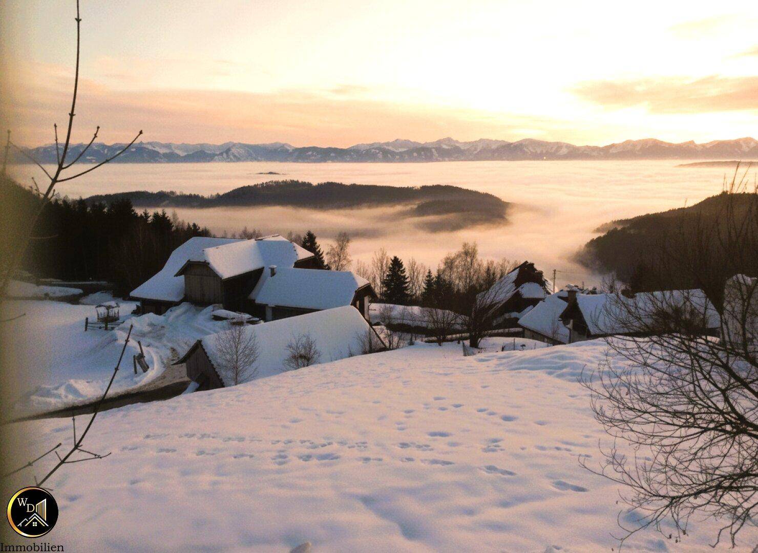 Malerische Winterlandschaft mit schneebedeckten Häusern und einem nebelverhangenen Tal bei Sonnenaufgang oder Sonnenuntergang.