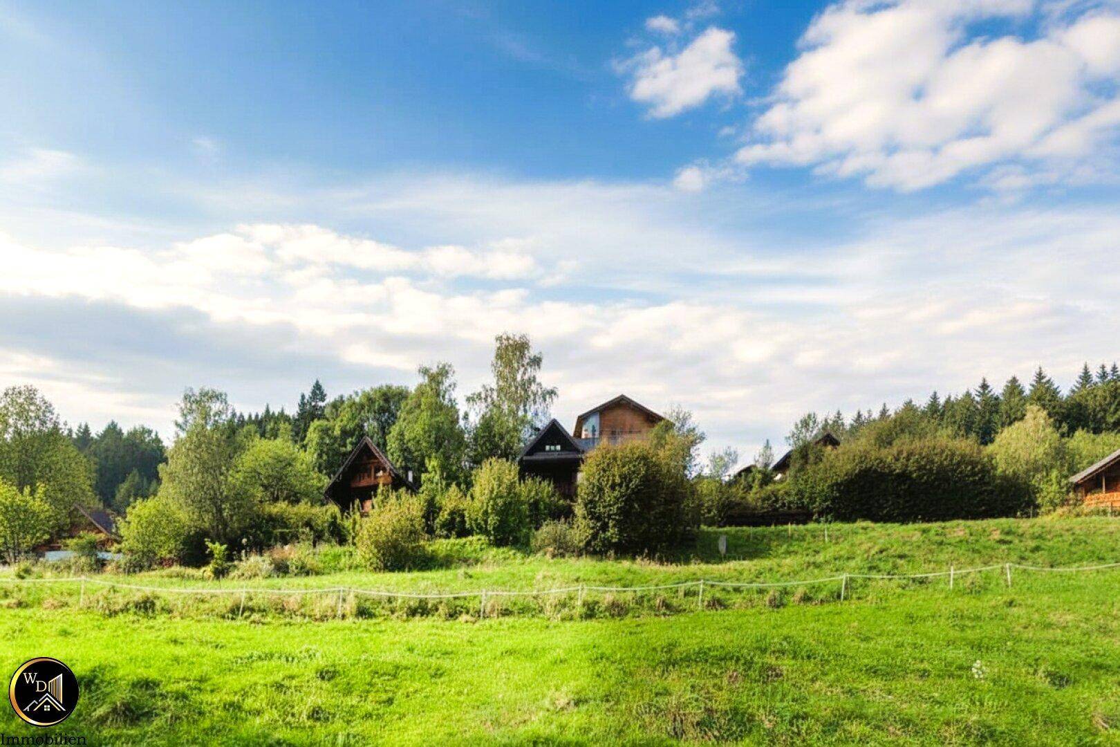 Idyllische ländliche Szene mit Häusern, umgeben von üppigem Grün und Bäumen unter einem bewölkten Himmel.