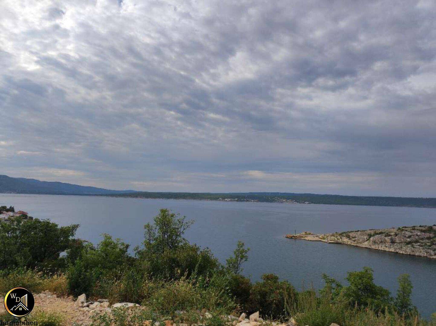 Aussicht auf das weite Meer mit felsigen Ufern und bewaldeten Hügeln am Horizont.