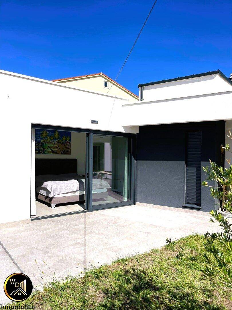 Moderne Hausfassade mit großen Glasschiebetüren, die zu einem Schlafzimmer und einer Terrasse führen.