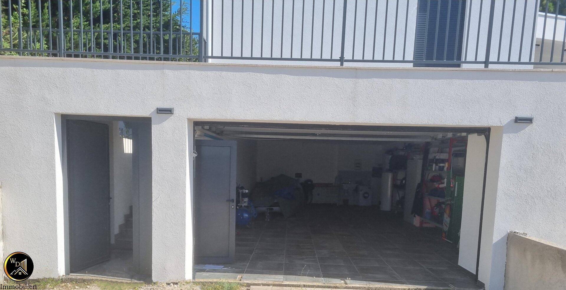 Eingang zur Garage mit geöffnetem Tor und Blick auf den gefliesten Innenraum.