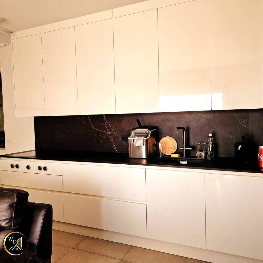 Elegante weiße Hochglanzküche mit dunkler Arbeitsplatte und integrierten Geräten.