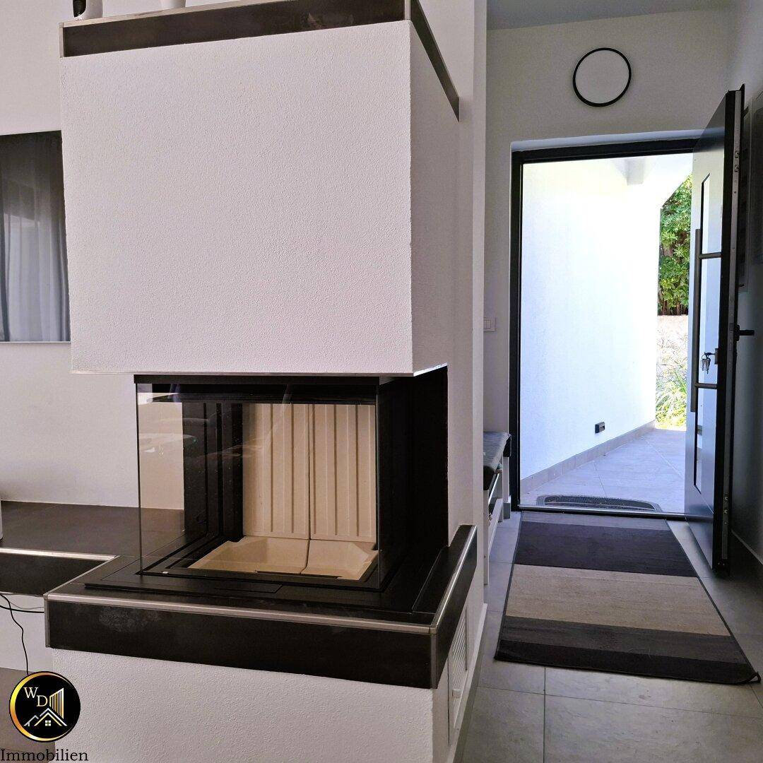 Moderner Kamin im Eingangsbereich, der den Übergang zum Wohnraum markiert.