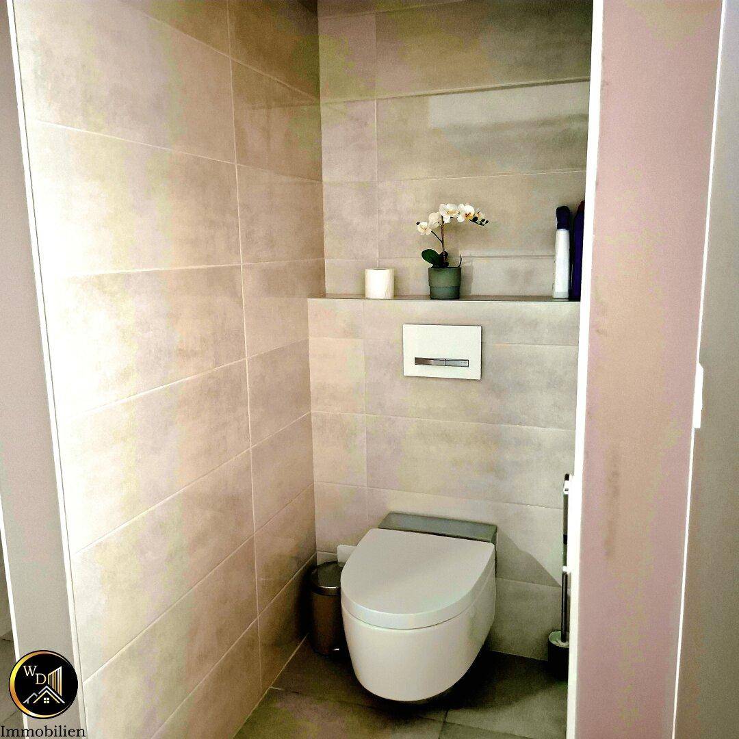 Modernes Wand-WC mit beigefarbenen Fliesen und einer Ablagefläche darüber.
