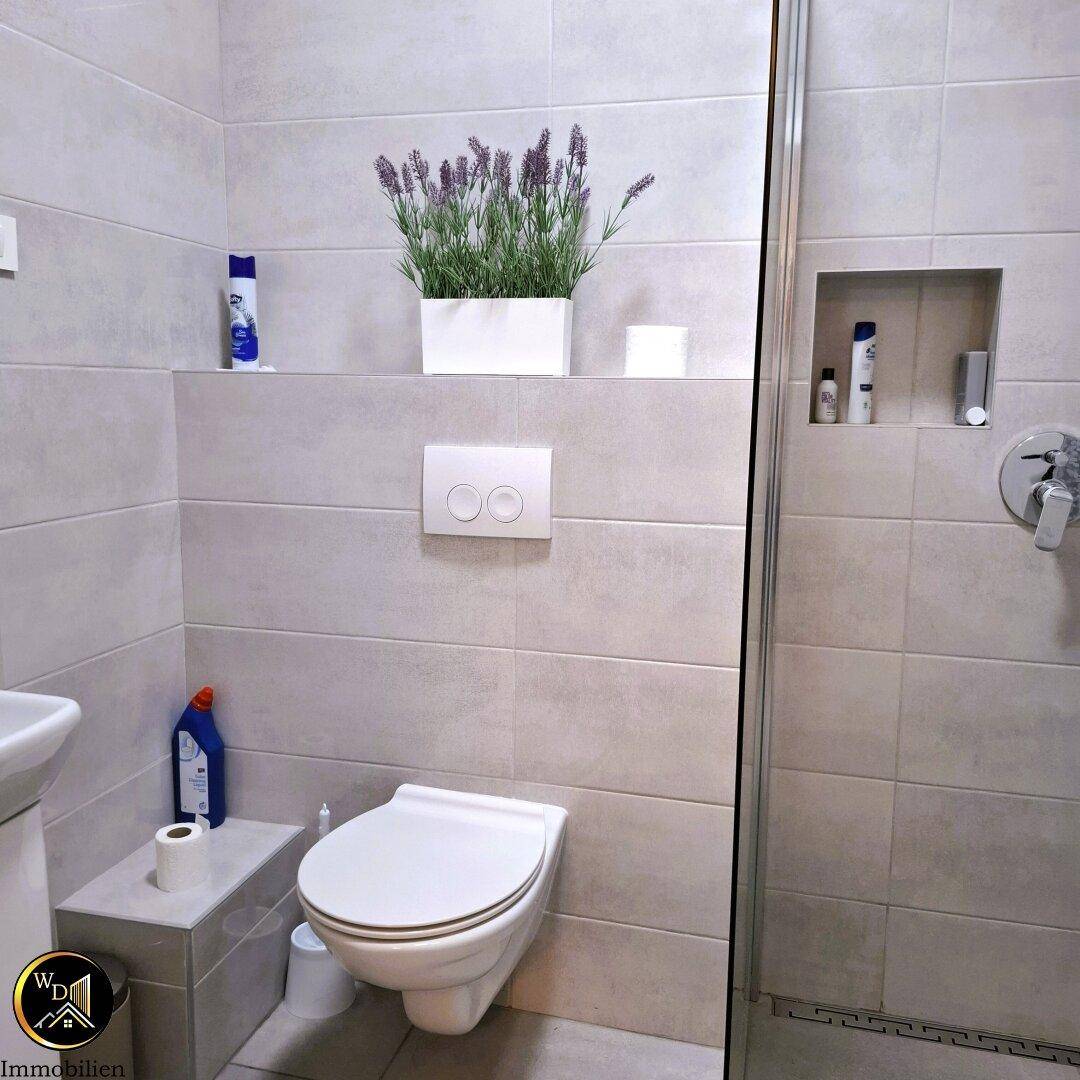 Modernes Badezimmer mit Wand-WC, Duschbereich und hellgrauen Fliesen.