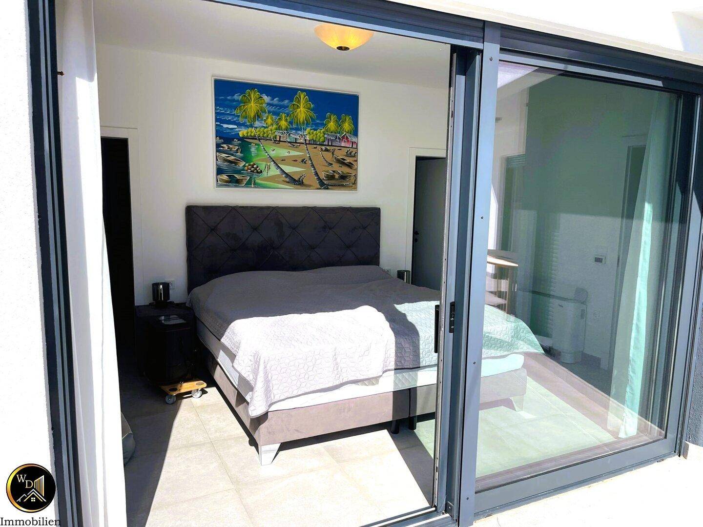 Gemütliches Schlafzimmer mit Doppelbett, Kunstwerk über dem Kopfteil und Zugang nach draußen.
