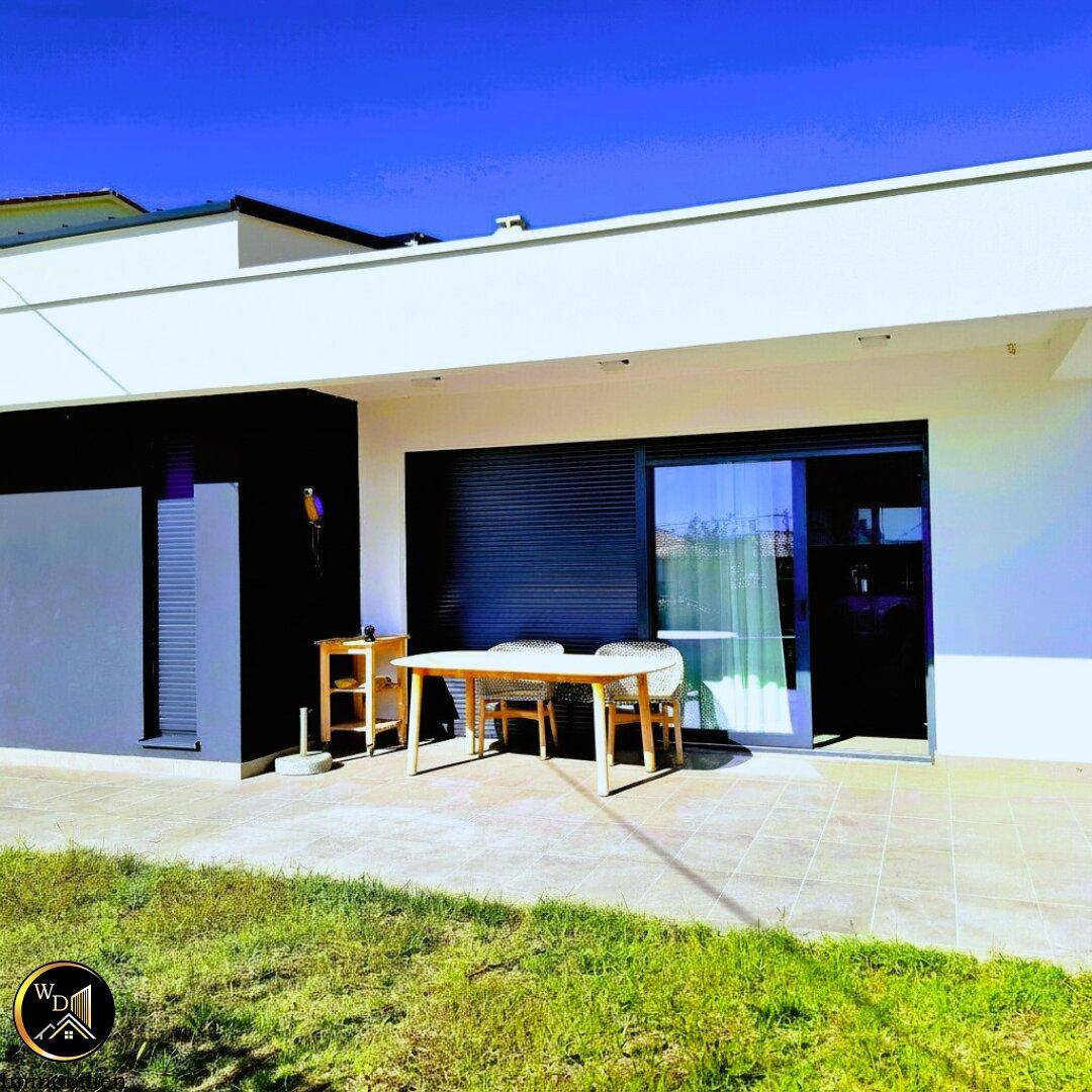 Moderne Hausfassade mit Terrasse, Esstisch im Freien und kleiner Rasenfläche.