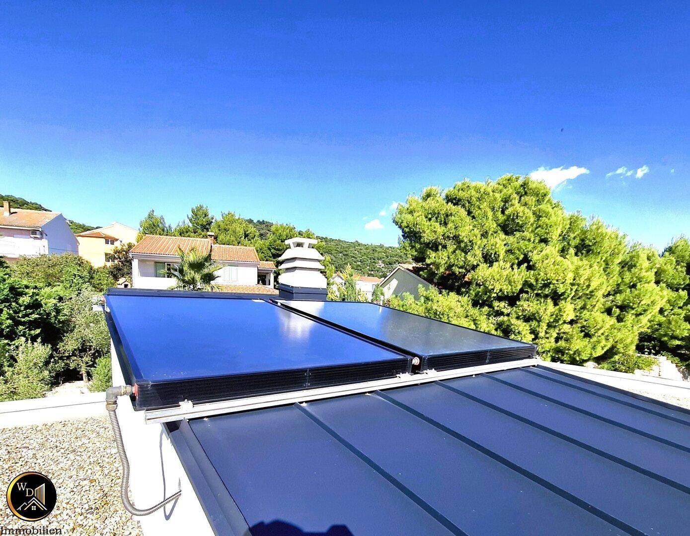 Solarpaneele auf dem Dach zur Energiegewinnung, umgeben von grünen Bäumen.
