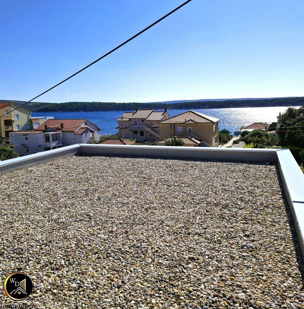 Dachterrasse mit Kiesbelag und weitem Blick auf das Meer und die umliegenden Häuser.