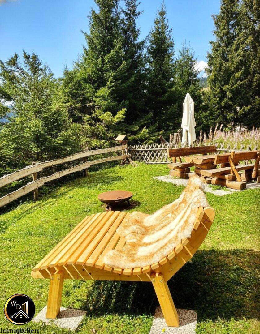 Gemütlicher Holzliegestuhl mit Fellauflage im grünen Garten, umgeben von Bäumen und Wiesen.