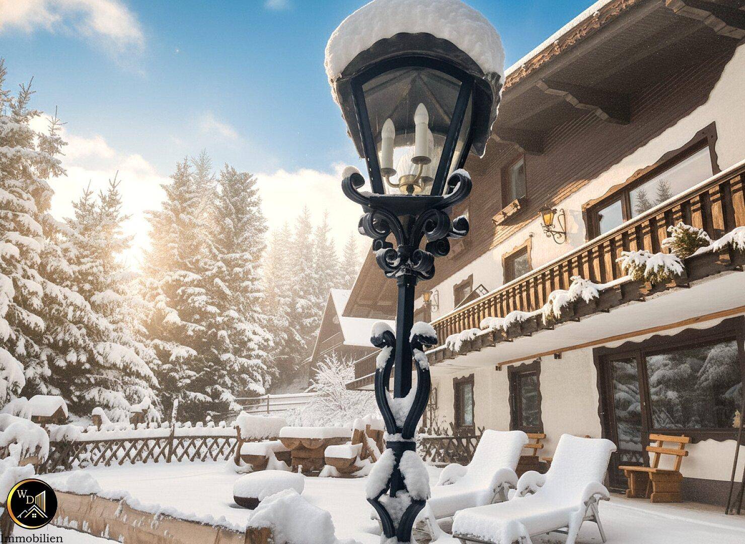 Winterliche Terrasse mit Schnee bedeckt, Gartenmöbeln und einer dekorativen Laterne vor verschneiter Landschaft.