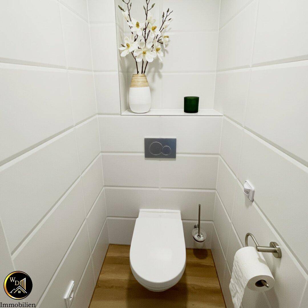 Modernes Gäste-WC mit weißen Wandfliesen und Holzboden, ausgestattet mit einem Wand-WC.