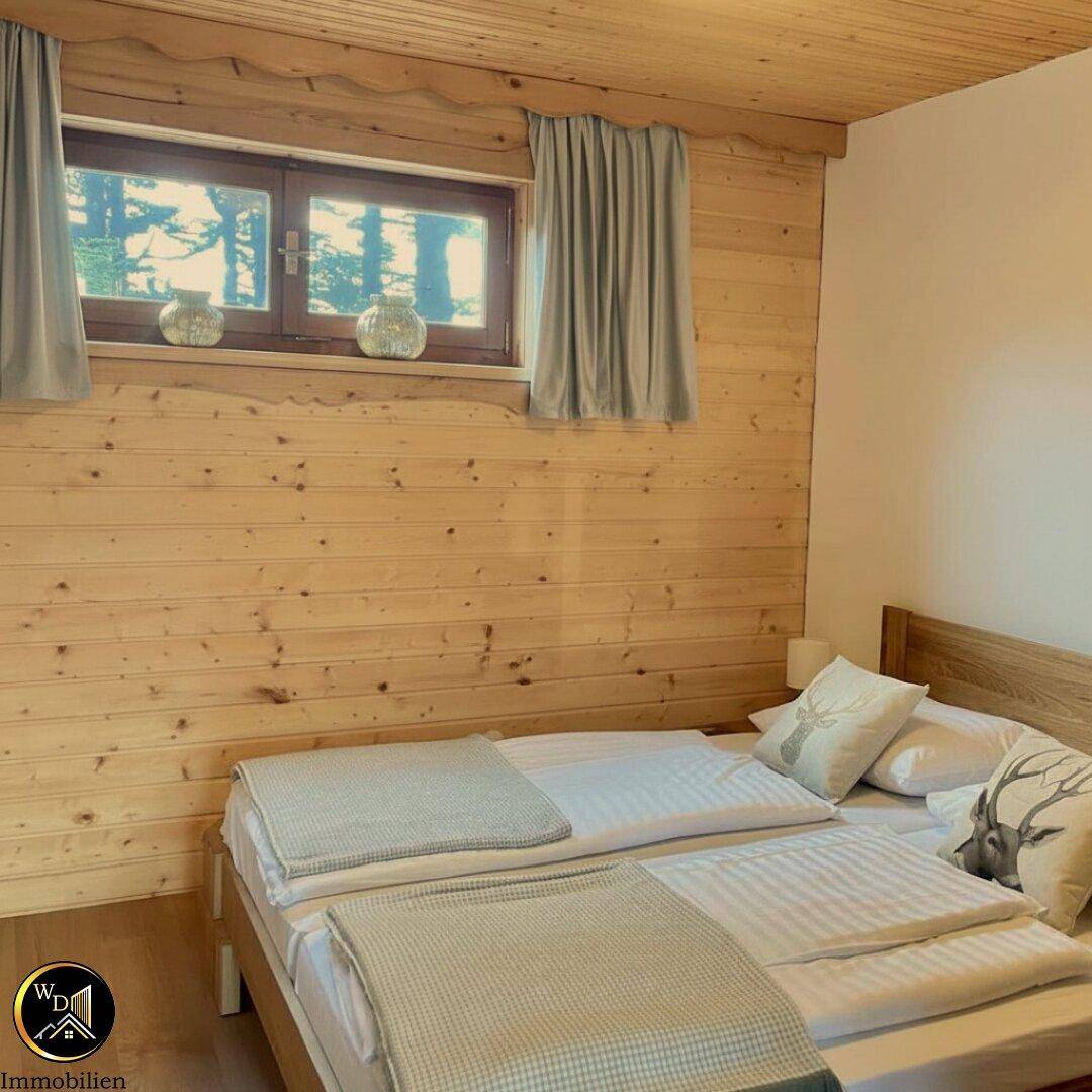 Helles Schlafzimmer mit Holzvertäfelung, Holzboden und Blick ins Grüne durch das Fenster.