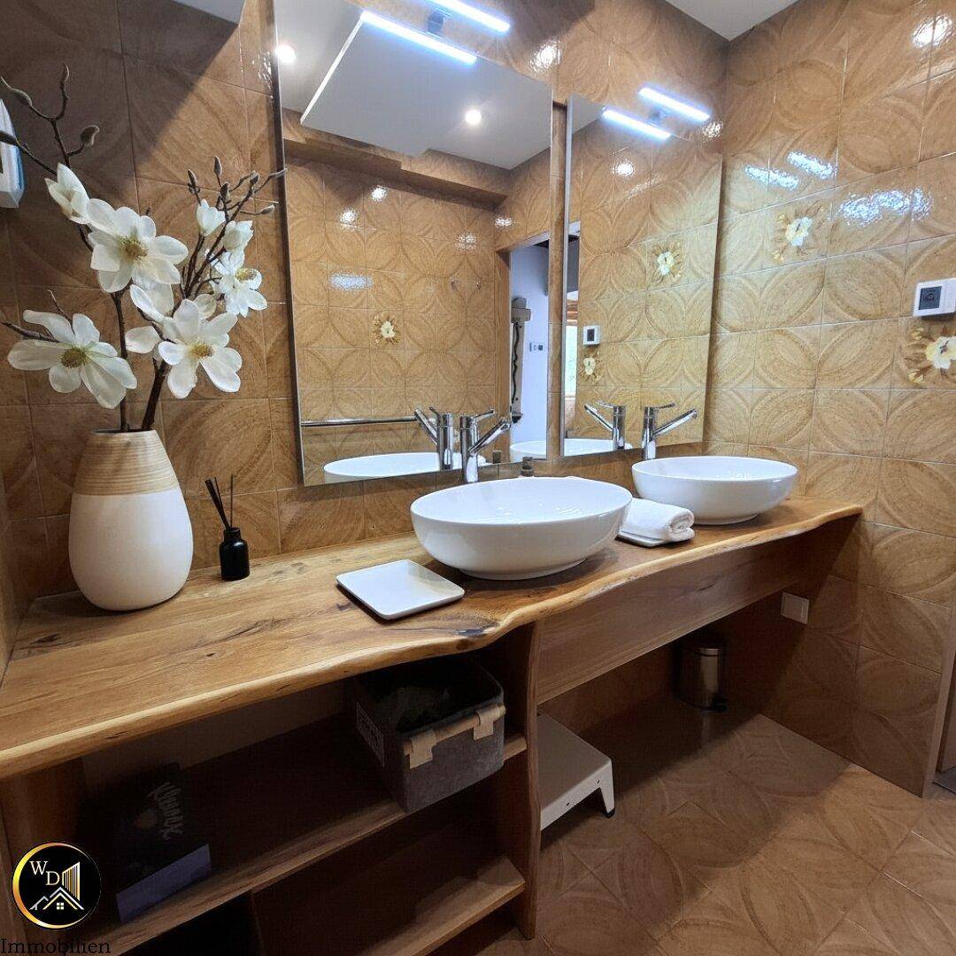 Modernes Badezimmer mit zwei Aufsatzwaschbecken auf einer Holzplatte und gemusterten Fliesen.