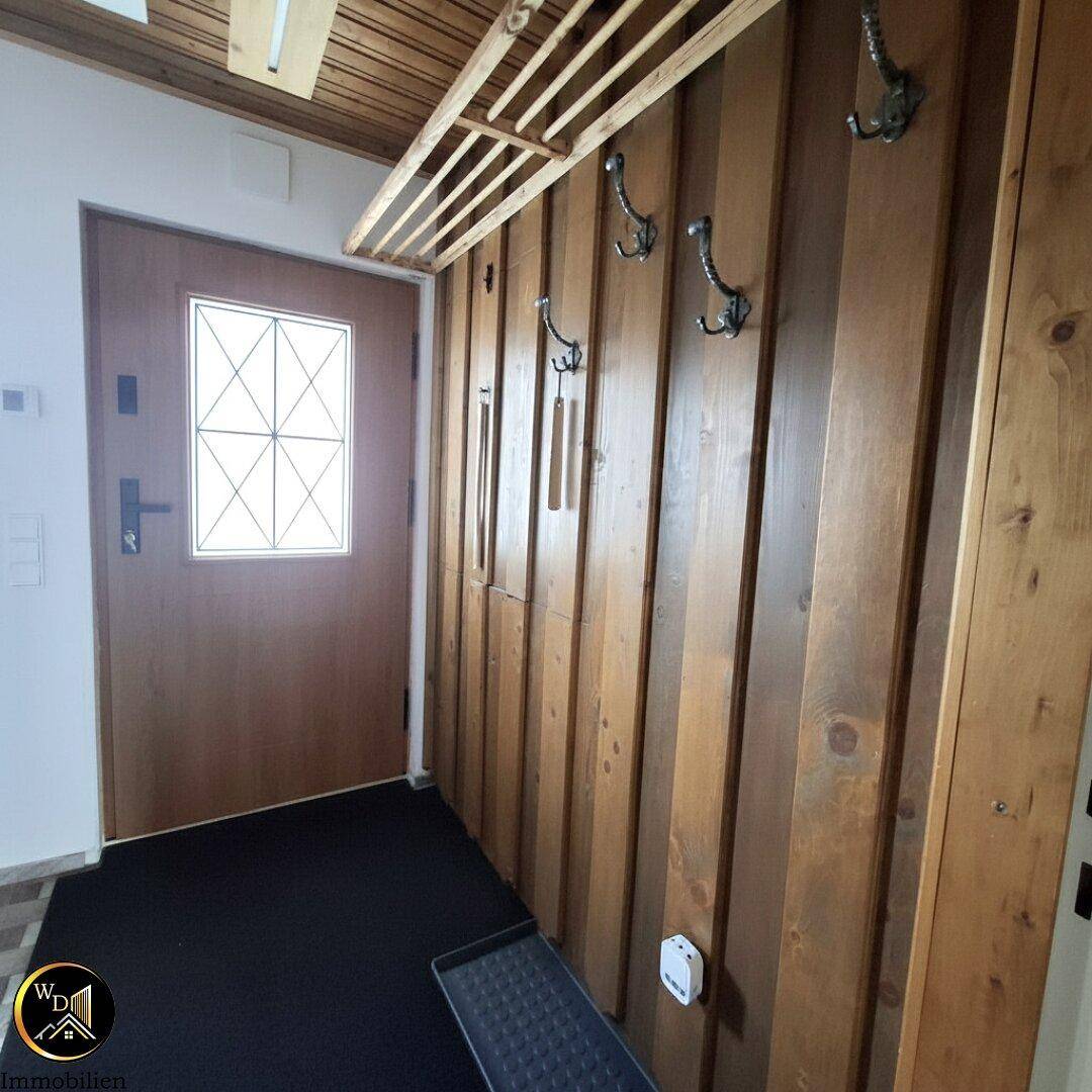 Gemütlicher Eingangsbereich mit Holzvertäfelung, Garderobe und dunklem Fußabtreter.