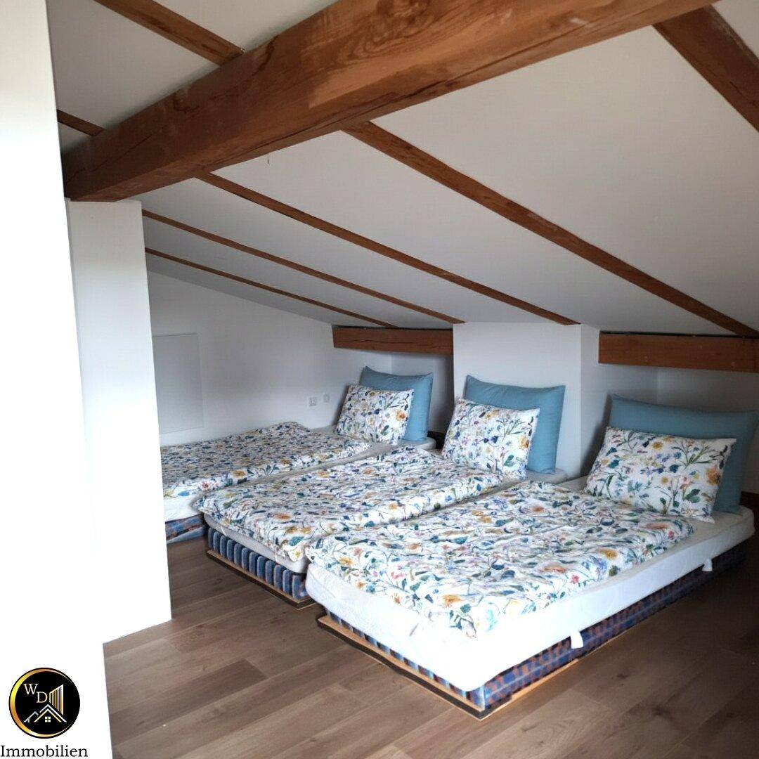 Geräumiges Schlafzimmer im Dachgeschoss mit mehreren Betten und sichtbaren Holzbalken.