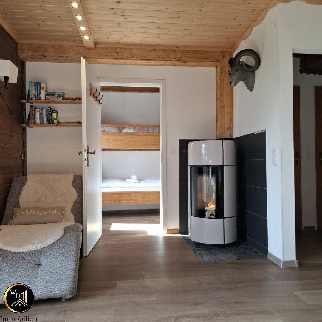 Wohnbereich mit modernem Kaminofen, Holzbalkendecke und Zugang zu einem Schlafzimmer.