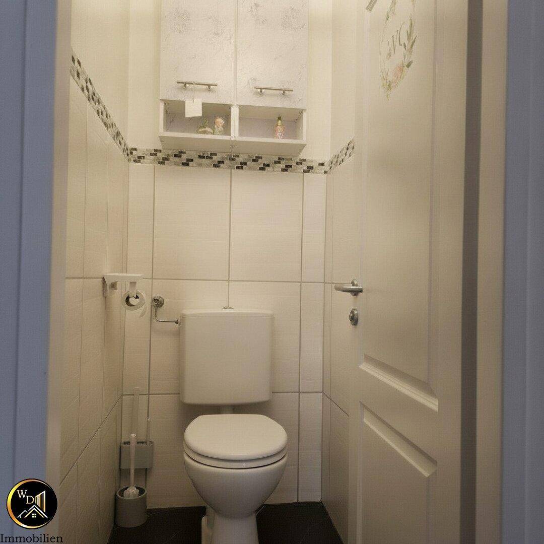 Kleines Gäste-WC mit Toilette, Fliesen und Hängeschrank.
