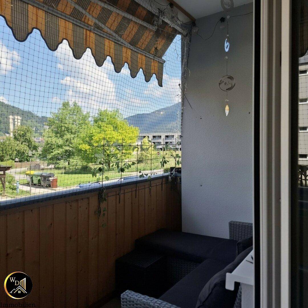 Balkon mit Markise, Sitzgelegenheiten und Blick auf Bäume und Berge.
