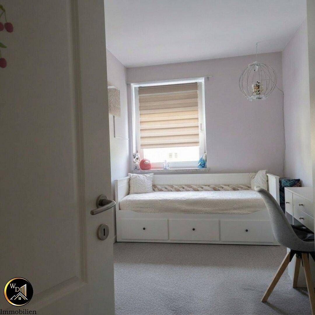 Helles Zimmer mit Tagesbett, Teppichboden und Fenster mit Jalousie.