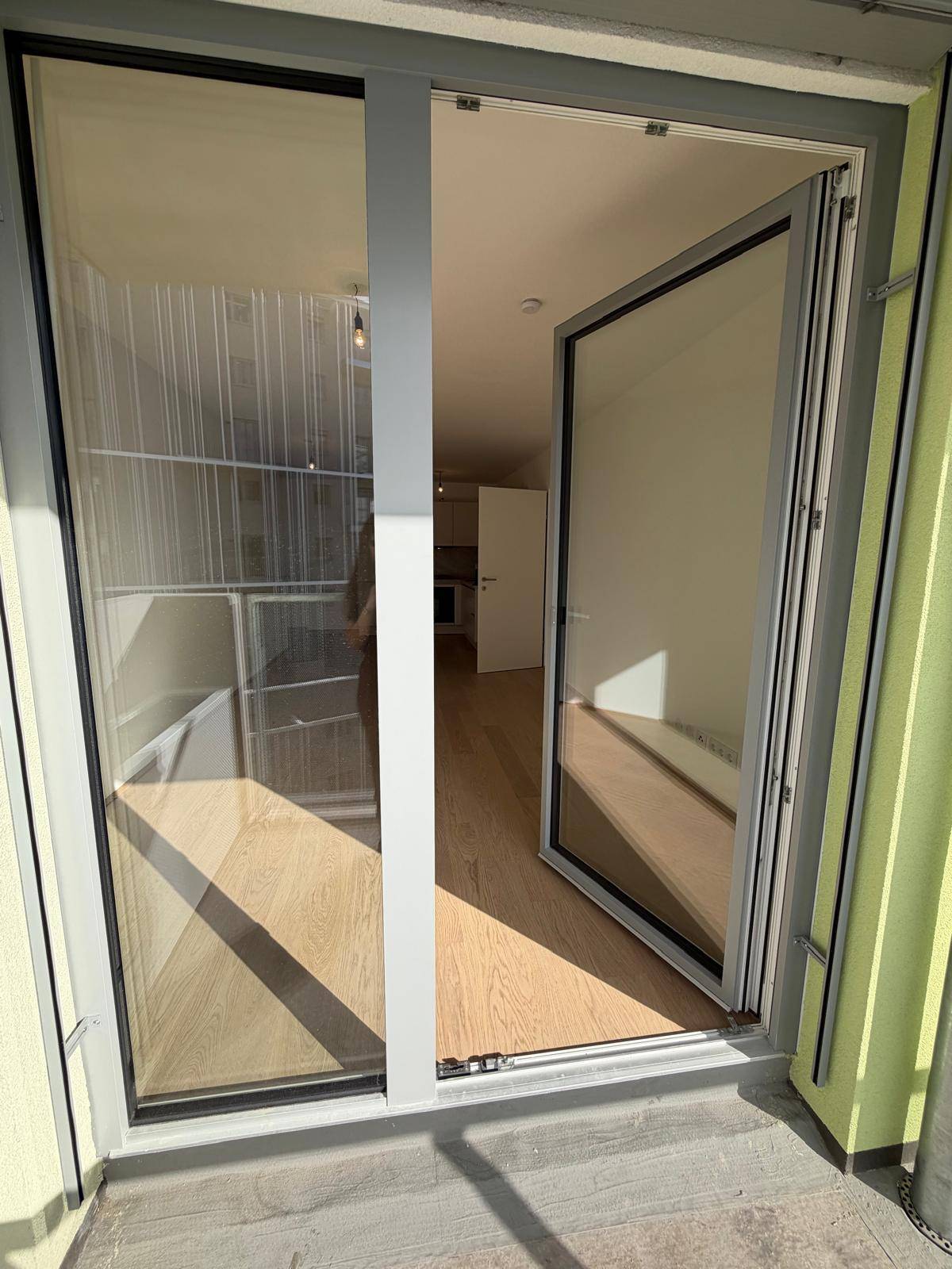 Blick vom Balkon in die helle Wohnung mit Holzboden und großen Glasfronten, die viel Licht hereinlassen.