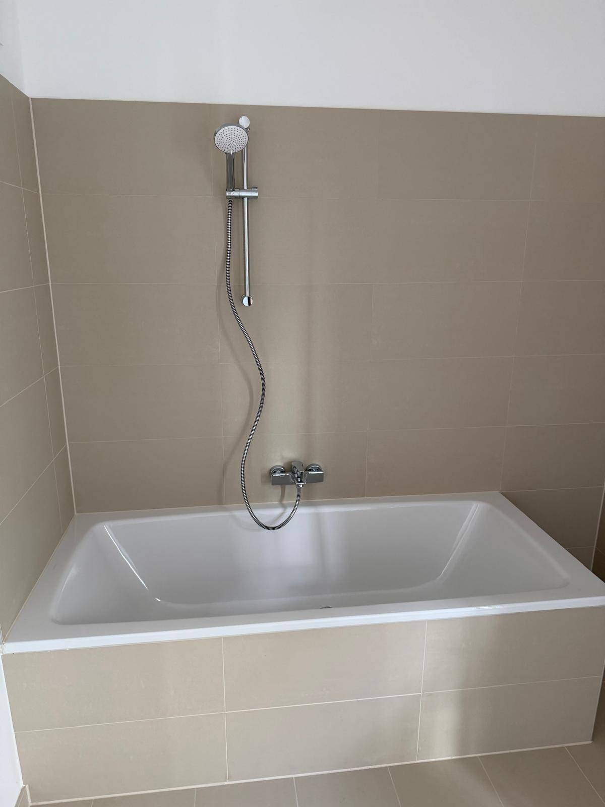 Detailansicht der Badewanne mit integrierter Duschfunktion und beigefarbenen Wandfliesen.