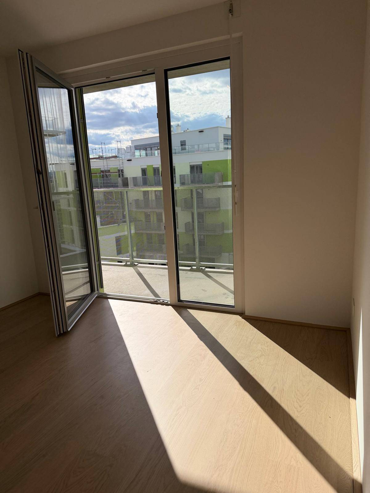 Große Glastür im Wohnbereich mit Blick auf moderne Wohngebäude und deren Balkone, die viel Licht spendet.