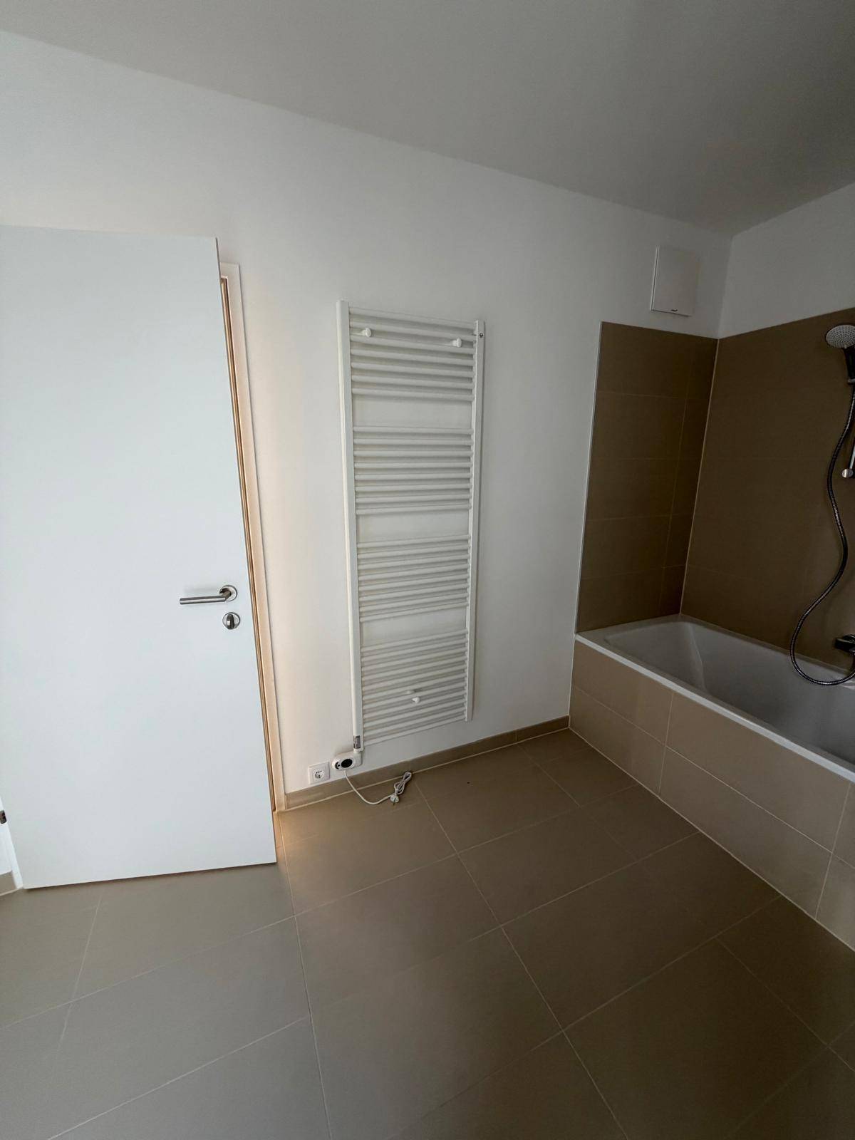Badezimmer mit beheiztem Handtuchhalter, weißer Tür und beigefarbenen Fliesen, die eine warme Atmosphäre schaffen.