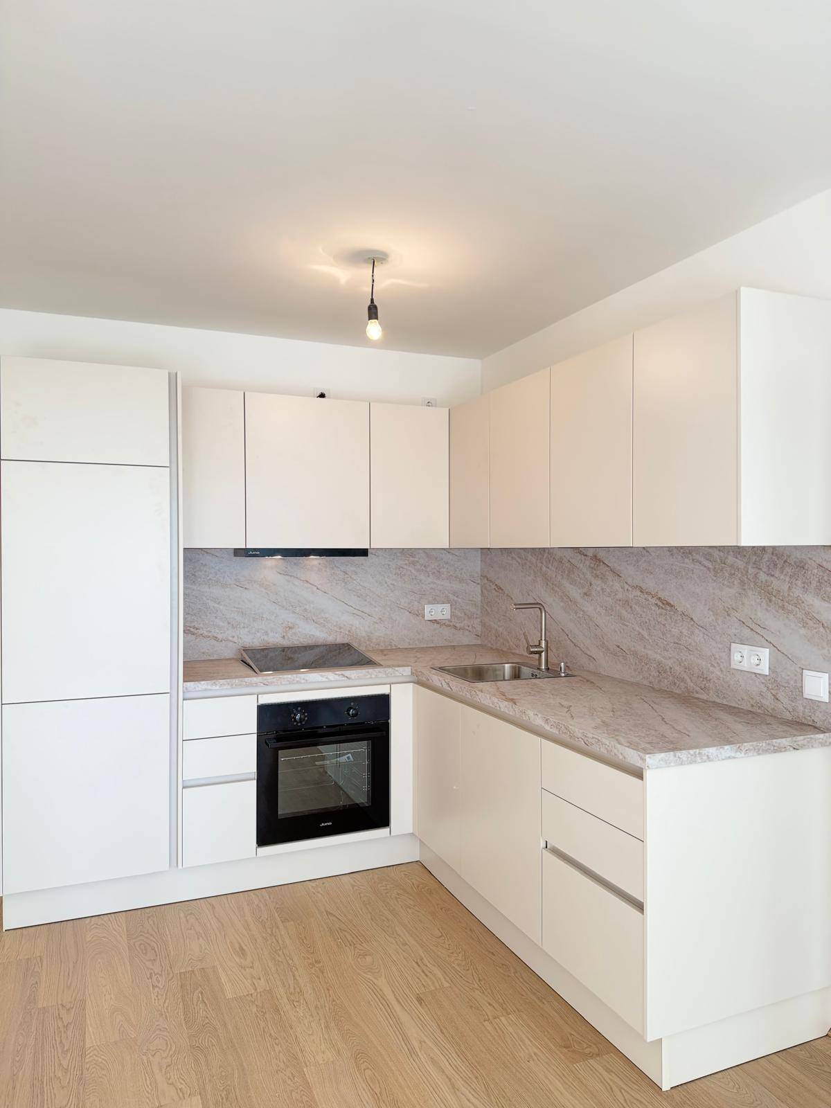 Moderne Einbauküche mit hellen Schränken, integriertem Backofen und gemusterter Arbeitsplatte auf Holzboden.