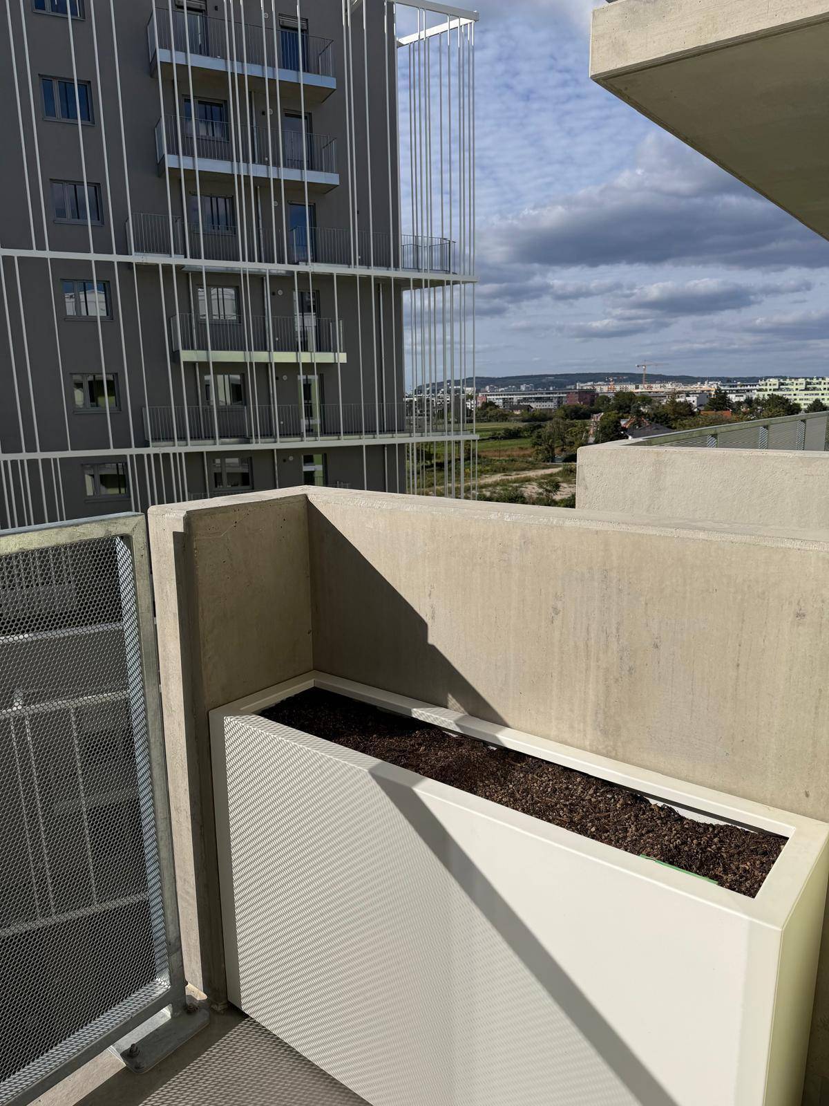 Balkon mit modernem Pflanzgefäß und weitem Blick über die Stadtlandschaft und angrenzende Gebäude.