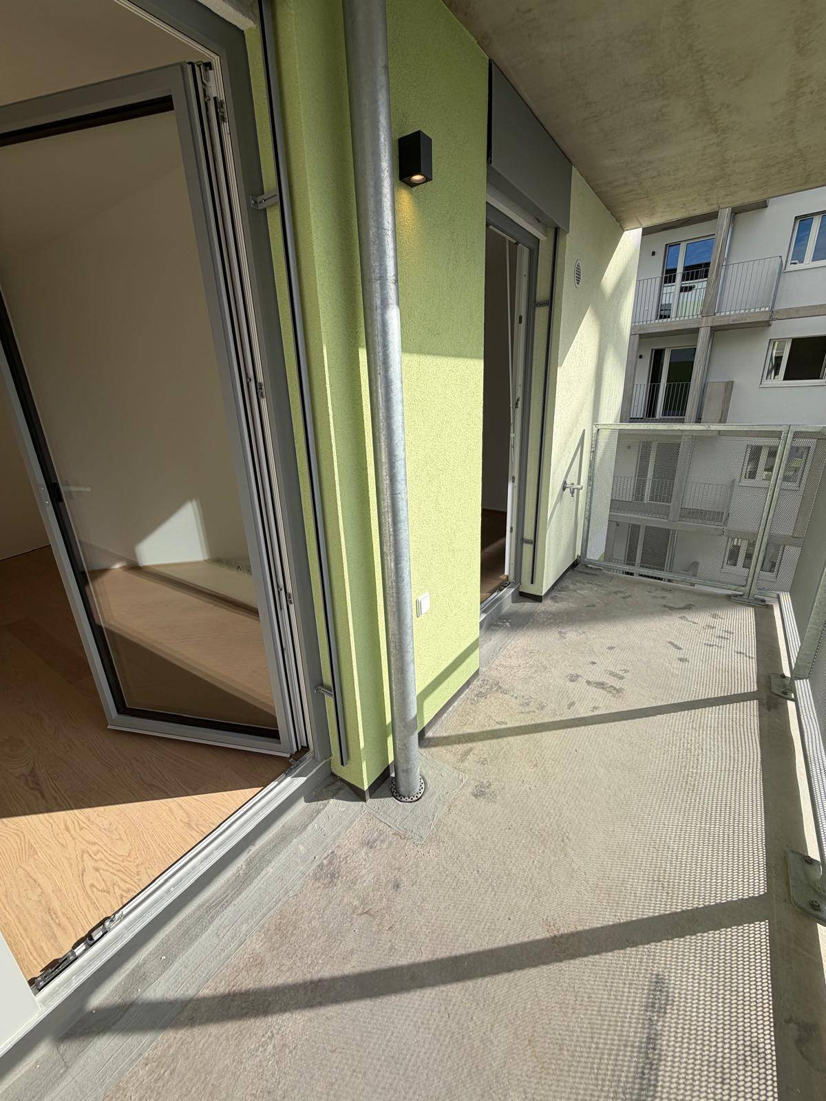 Geräumiger Balkon mit hellgrüner Wand und moderner Metallbrüstung, der einen Außenbereich bietet.