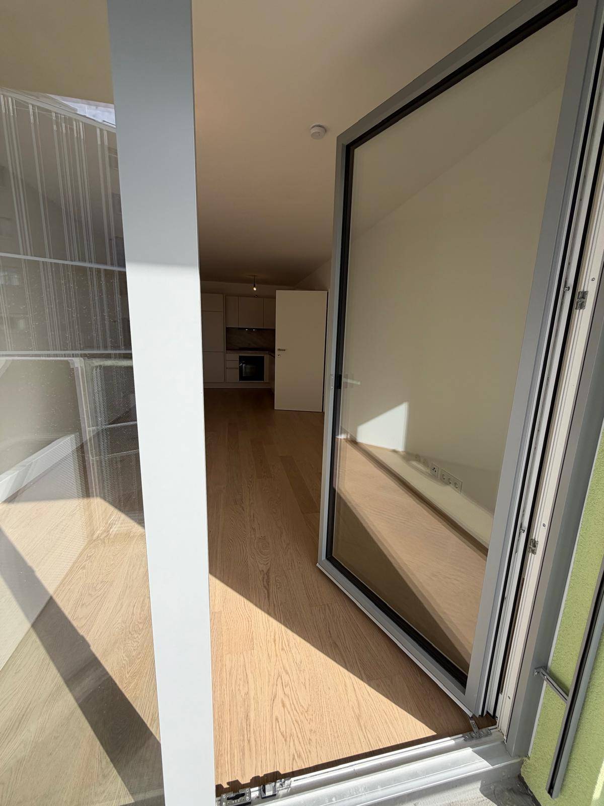 Blick vom Balkon in den hellen Innenraum der Wohnung mit Holzboden und offener Gestaltung.
