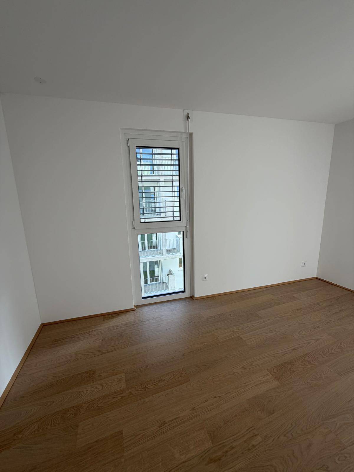 Hohes Fenster im Schlafzimmer mit Blick auf den Innenhof oder angrenzende Gebäudeteile, das Tageslicht spendet.