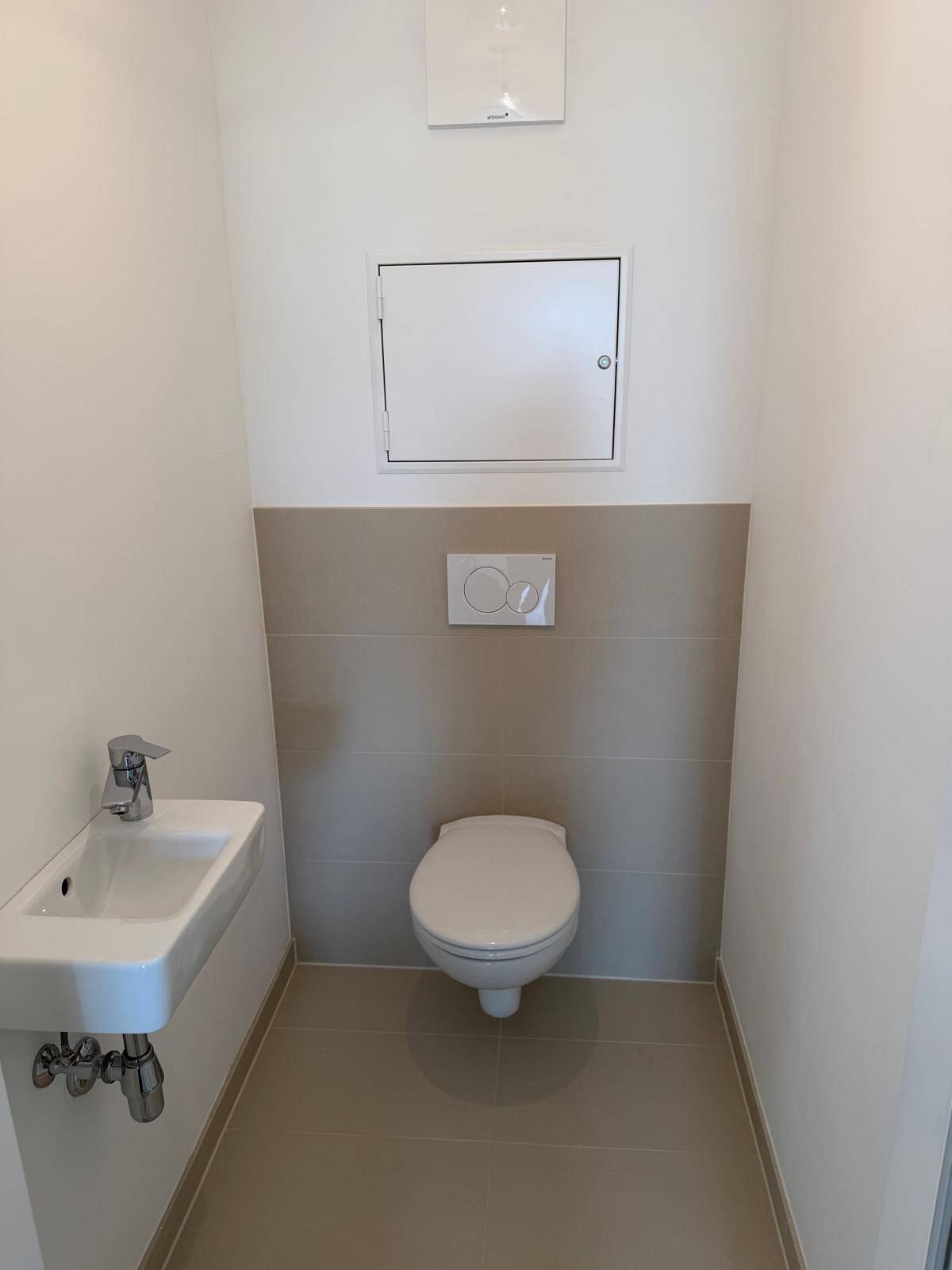 Modernes Gäste-WC mit wandhängender Toilette, kleinem Waschbecken und beigefarbenen Fliesen.