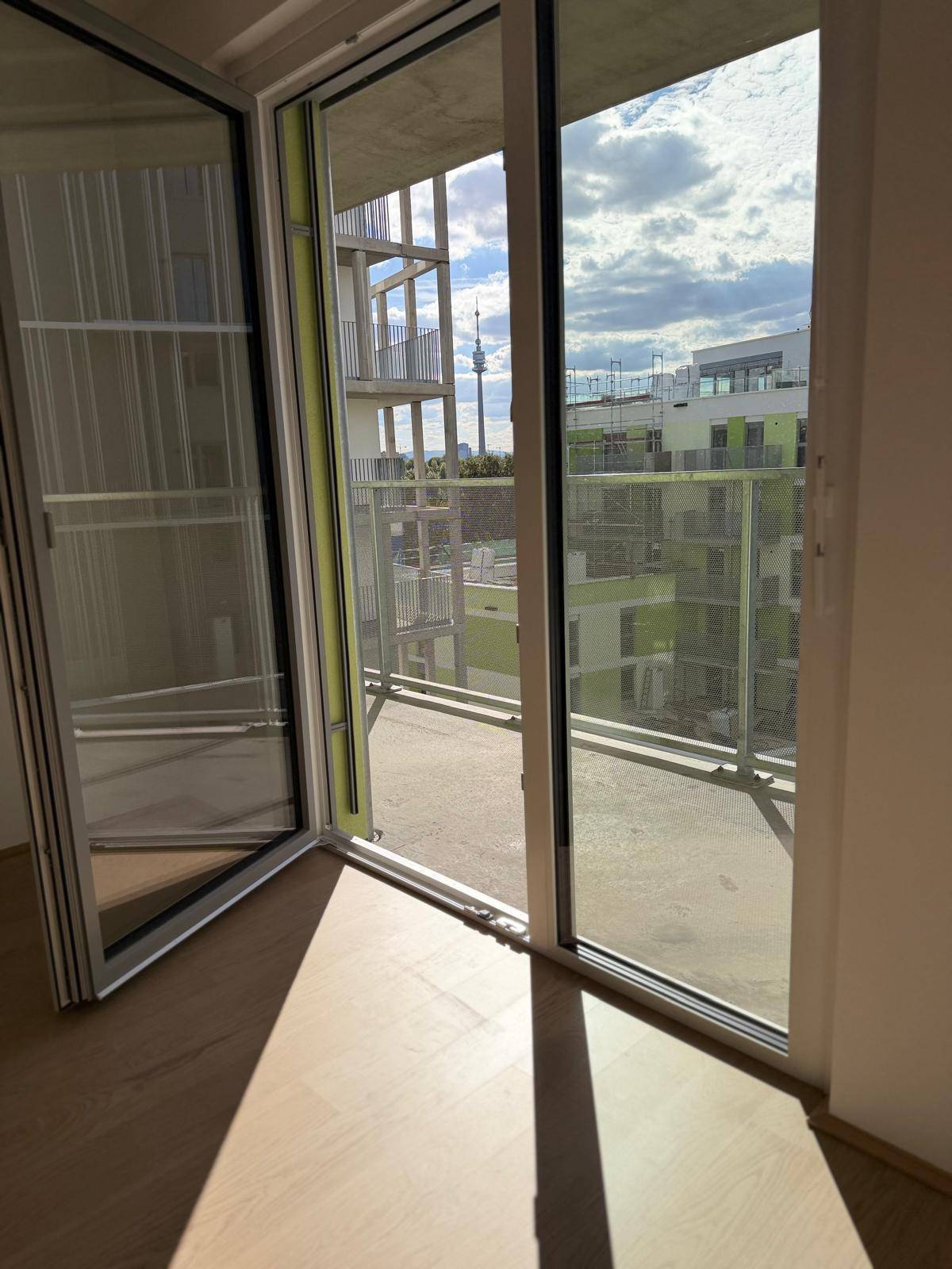 Blick durch die offene Balkontür auf den Balkon und die Stadtlandschaft mit einem markanten Turm am Horizont.