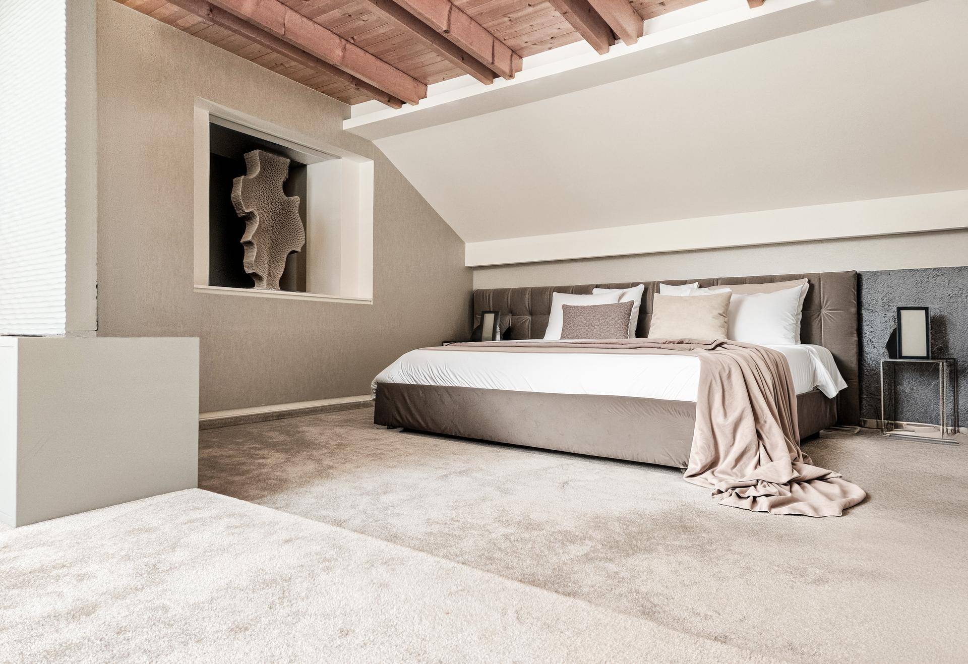 Elegantes Schlafzimmer im Dachgeschoss mit Teppichboden, Holzbalken und stilvoller Einrichtung.