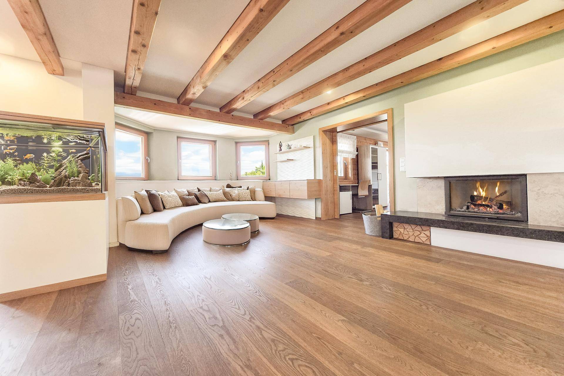 Gemütliches Wohnzimmer mit Holzbalkendecke, Kamin und einem großen Aquarium als Blickfang.