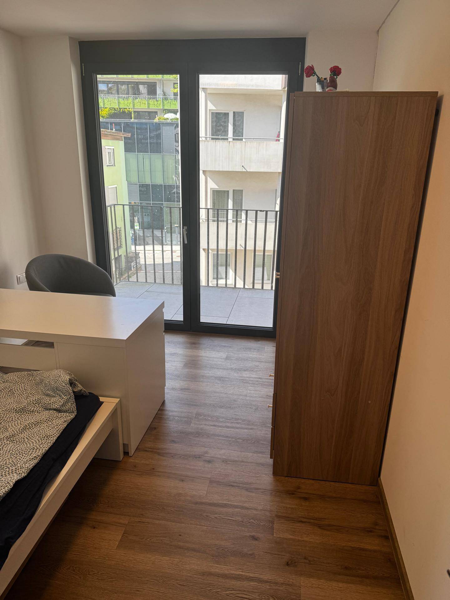 Große Fensterfront im Schlafzimmer bietet Blick auf die umliegenden Gebäude und den Balkon.