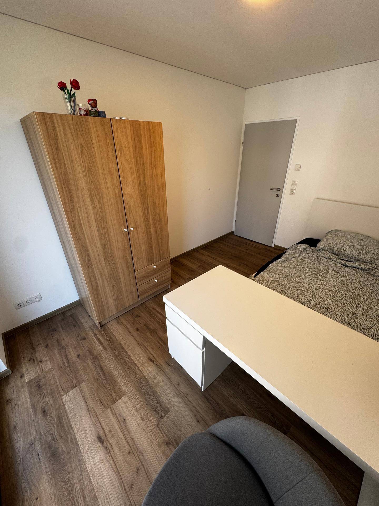 Schlafzimmer mit Holzboden, Schreibtisch und einem großen Kleiderschrank, der viel Stauraum bietet.
