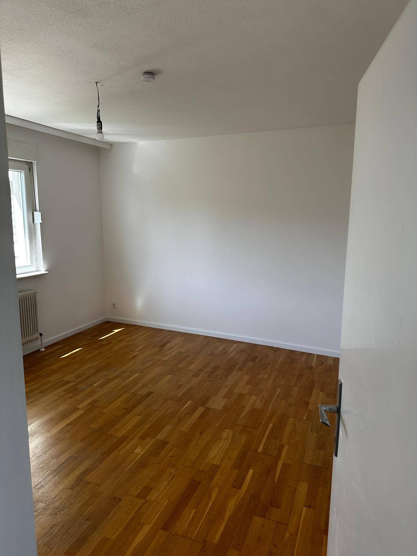 Geräumiges Schlafzimmer mit hellem Parkettboden und viel Tageslicht durch das Fenster.