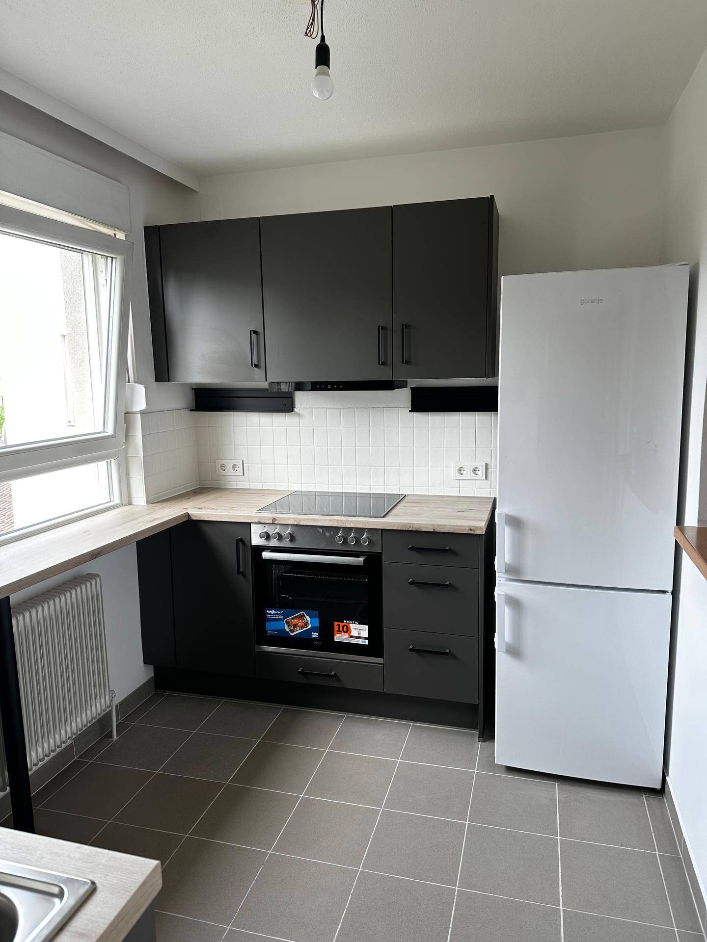 Moderne Küche mit dunklen Schränken, heller Arbeitsplatte, Induktionskochfeld und weißem Kühlschrank.