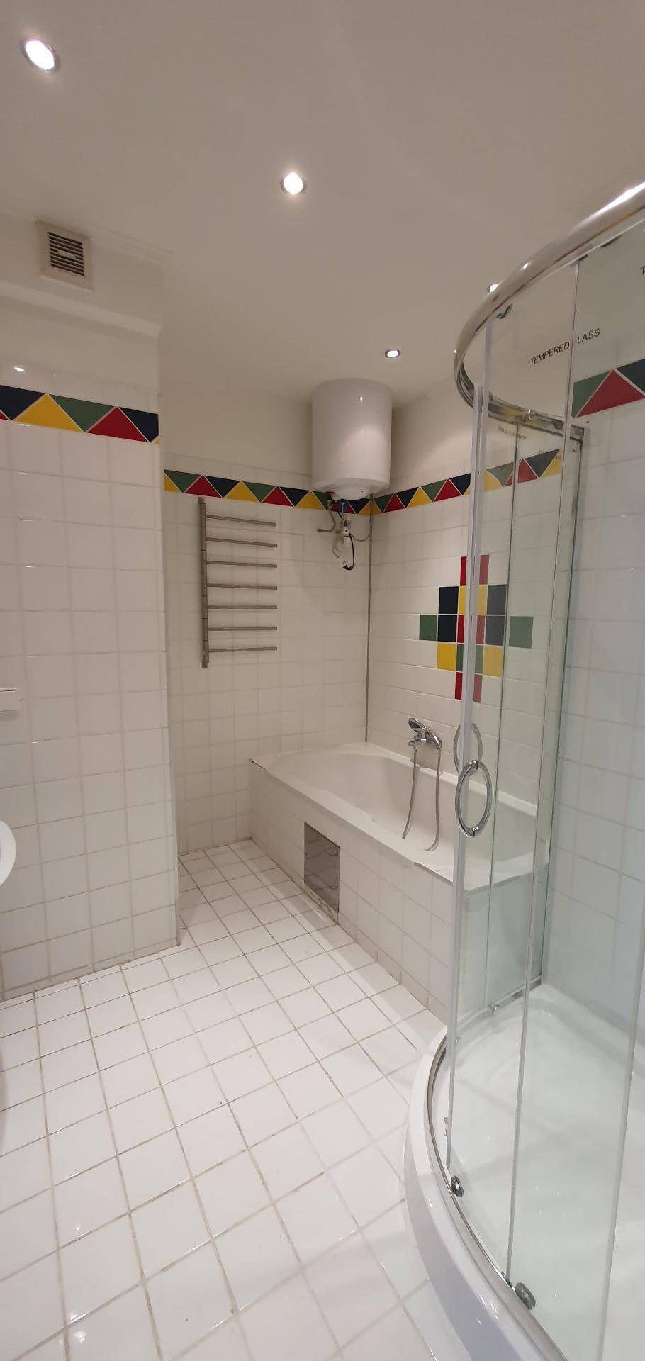 Badezimmer mit Badewanne, Duschkabine und farbigen Akzentfliesen an den Wänden.