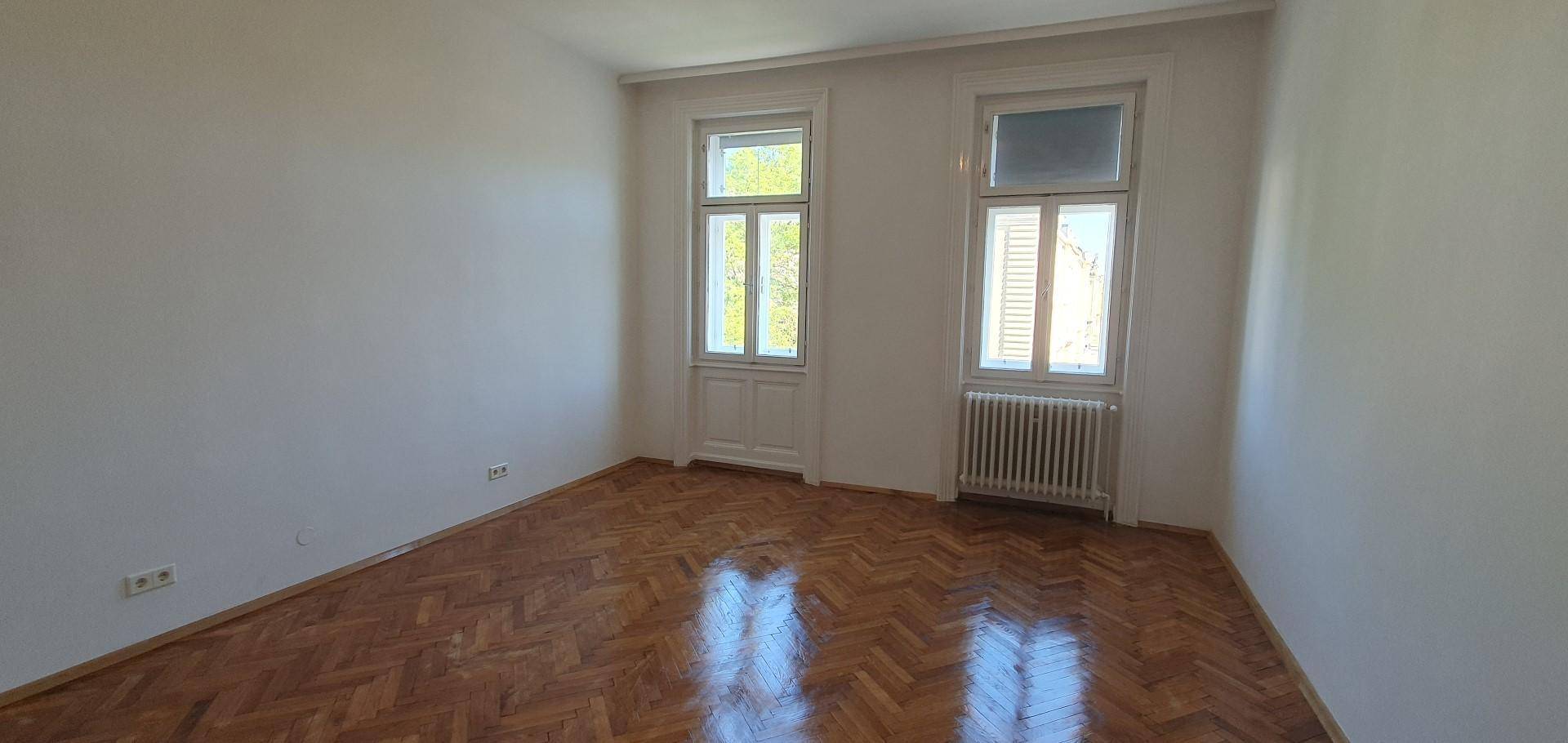 Helles Schlafzimmer mit Fischgrätparkett und zwei Fenstern, die den Raum mit Licht durchfluten.