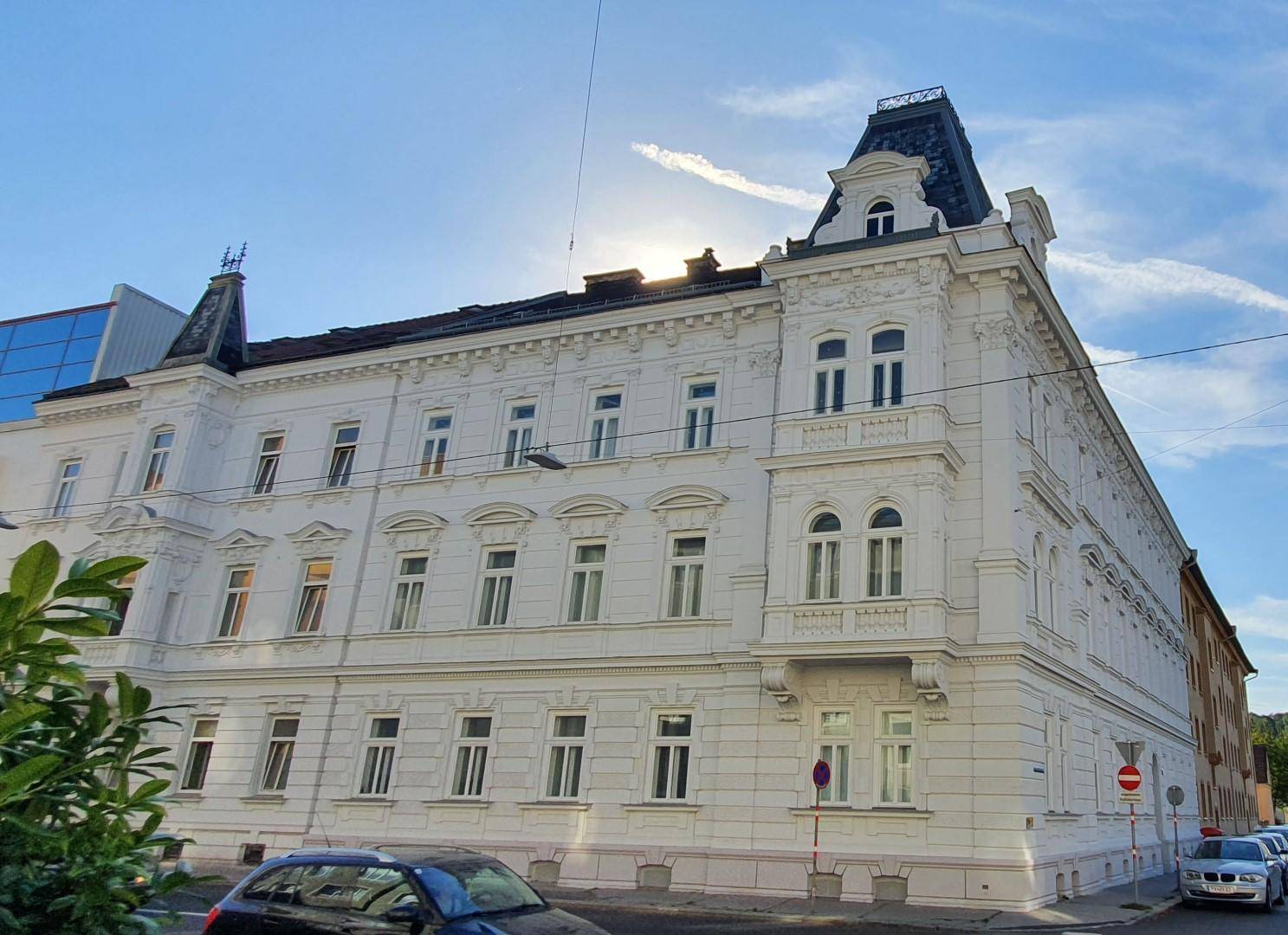 Historisches Gebäude mit eleganter weißer Fassade und klassischen architektonischen Details unter blauem Himmel.