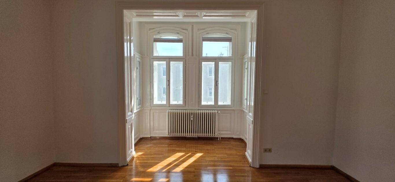Heller Raum mit Holzboden und einem großen Fensterbereich, der viel Sonnenlicht hereinlässt.