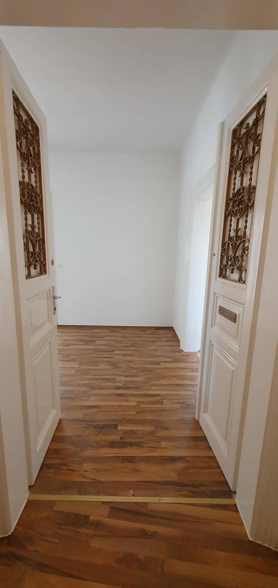 Heller Flur mit Holzboden und verzierten Doppeltüren, die in einen weiteren Raum führen.