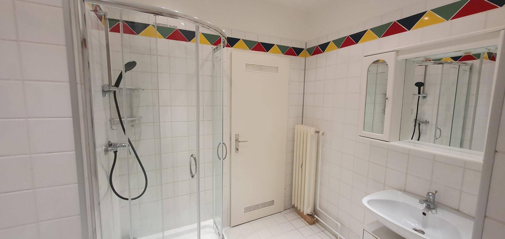 Badezimmer mit Duschkabine, Waschbecken und Spiegel, dekoriert mit farbigen Fliesen.