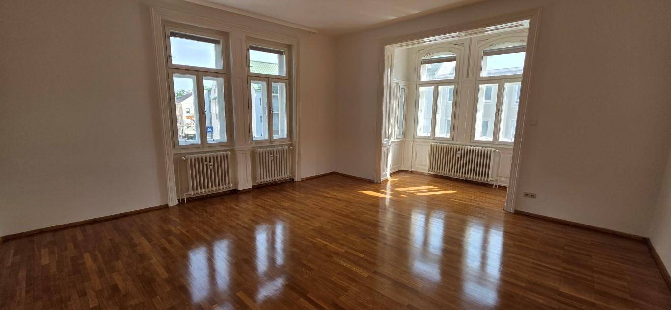 Großes, helles Wohnzimmer mit Holzboden und hohen Fenstern, die viel Licht spenden.